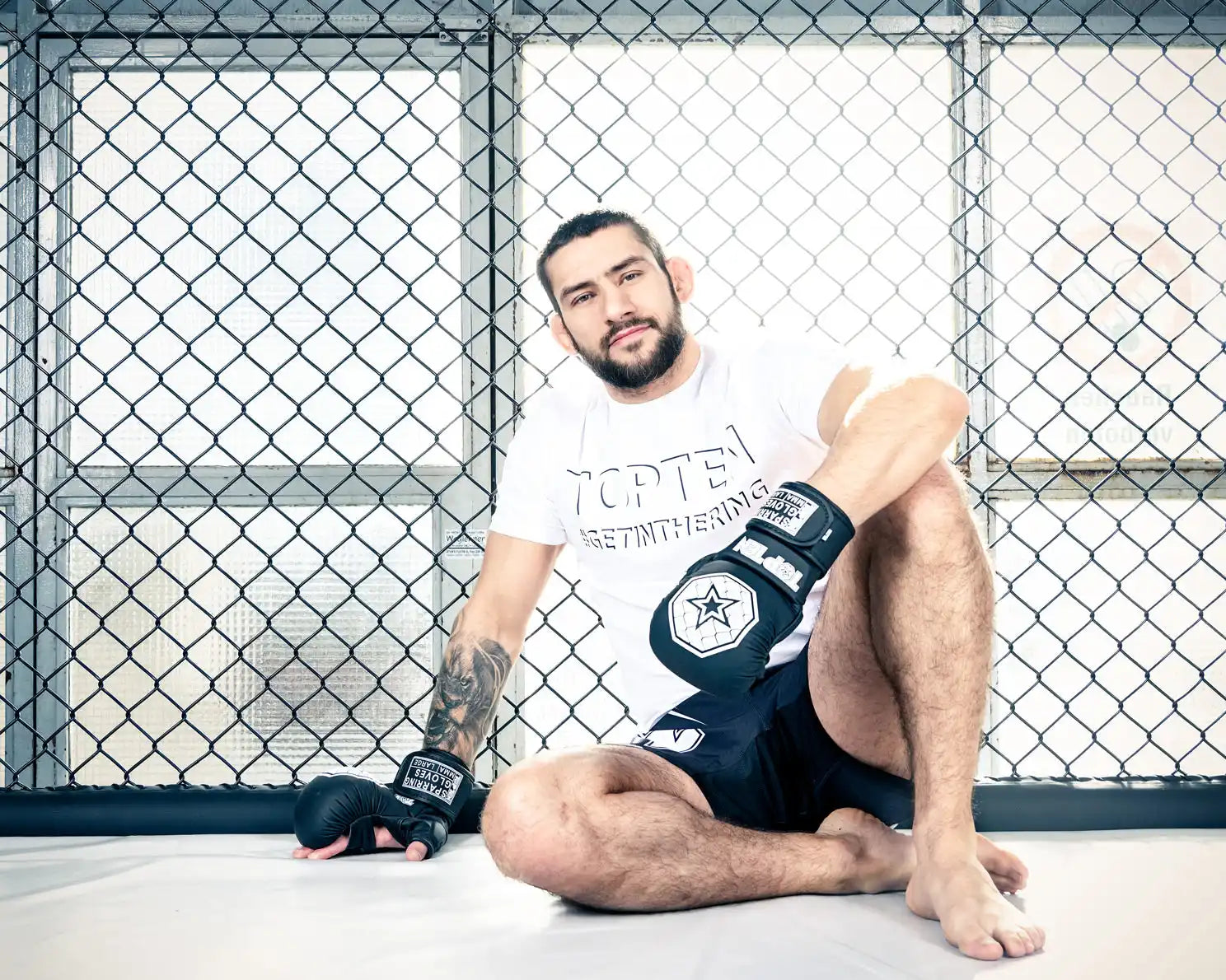 A male mixed martial arts (MMA) fighter in a white t-shirt, black shorts, and black MMA gloves.